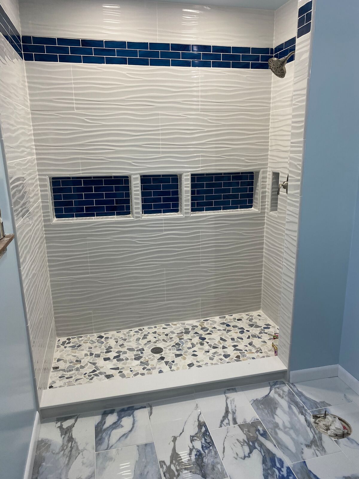 Tiled shower with wave-pattern wall tile, blue glass accents and pebble floor
