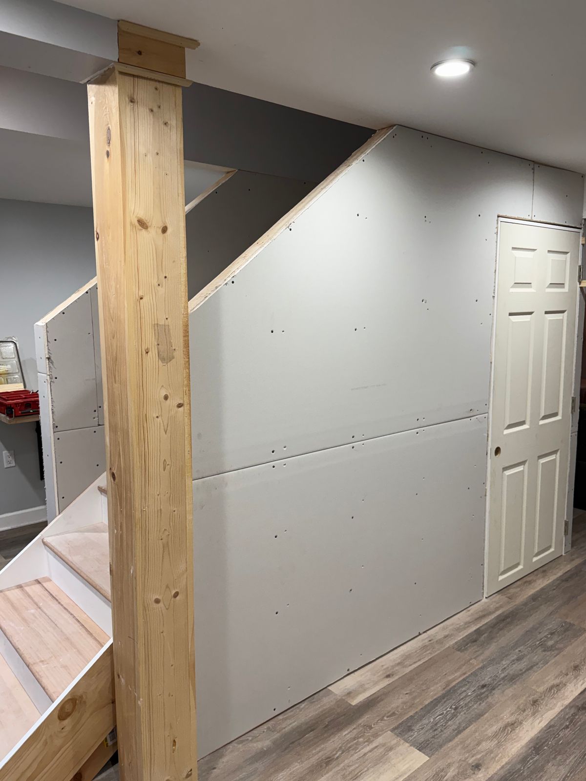 Basement stairway with drywall, wood post and plank flooring